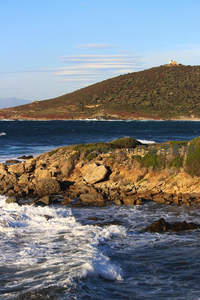 礁石海岸边浪花飞溅，远山灯塔静守海天一色