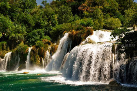 阳光下层叠瀑布倾泻入碧绿潭水