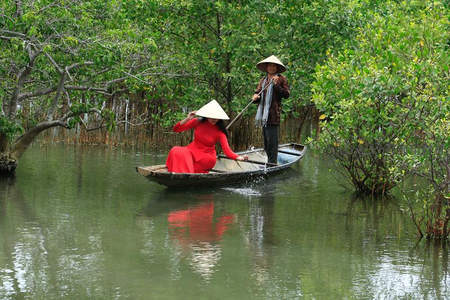 红裙女子泛舟绿林水道，传统斗笠显风情