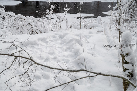 河岸雪堆枯枝点缀冬日河景
