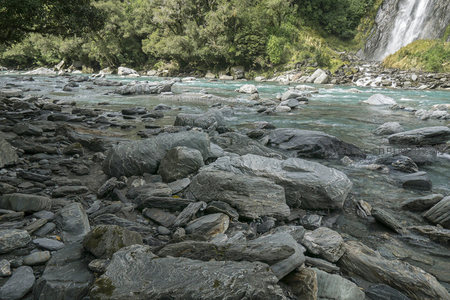 瀑布飞流直下汇入布满岩石的碧绿河谷