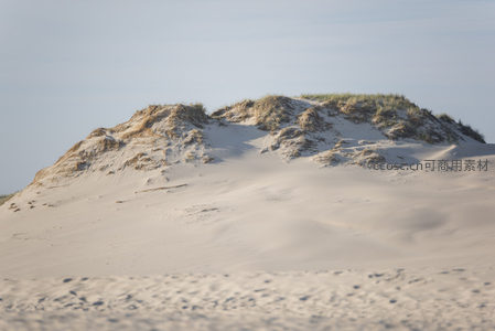 被绿草覆盖的沙丘在蓝天映衬下静谧优美