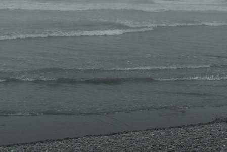 灰蒙海浪轻拍卵石滩岸