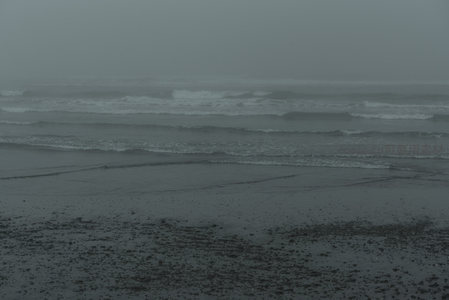 灰蒙海面波涛涌动，湿沙映衬寂寥之美