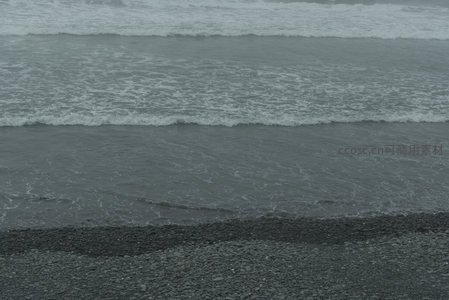灰调海浪轻抚黑色卵石滩，节奏舒缓