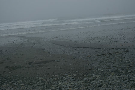 雾霭笼罩的静谧海岸，浪花轻拍卵石滩