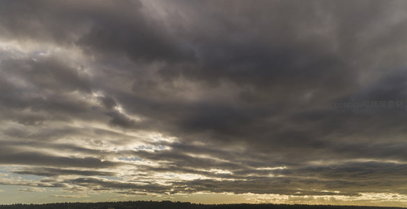 低空密布乌云缝隙中透出柔和夕阳光芒的景象