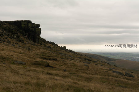 荒野山丘上的巨大岩层与远方城市天际线