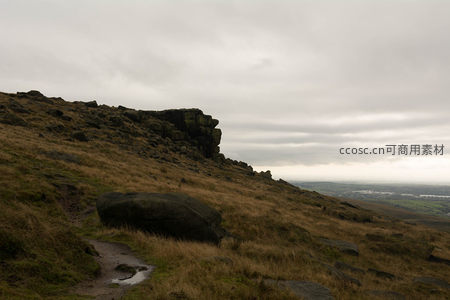 雨后湿滑小径旁的巨石与远处朦胧城镇