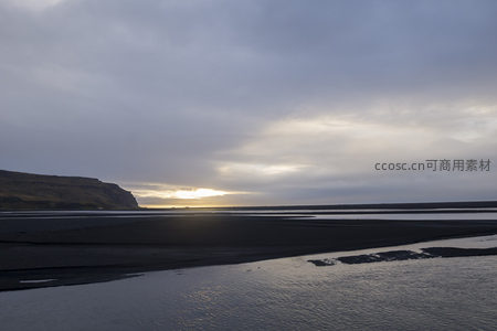 夕阳破云而出，照亮黑沙滩与海面
