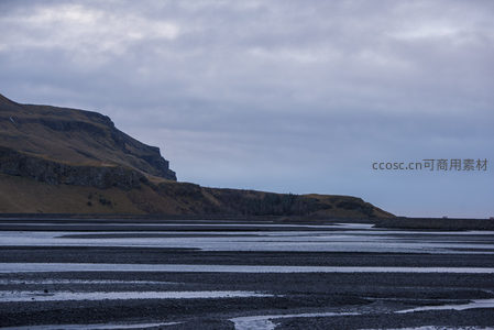 黑沙海岸线延伸，层叠水洼映灰蓝天空