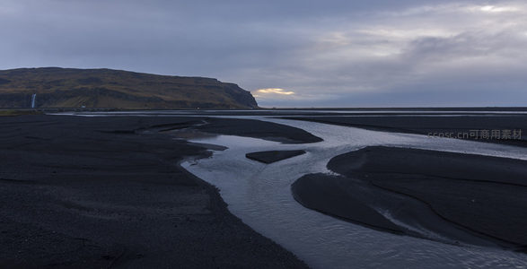 黑沙河床与远山瀑布的黄昏剪影