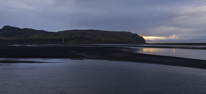 暮色中的黑沙滩与远山剪影