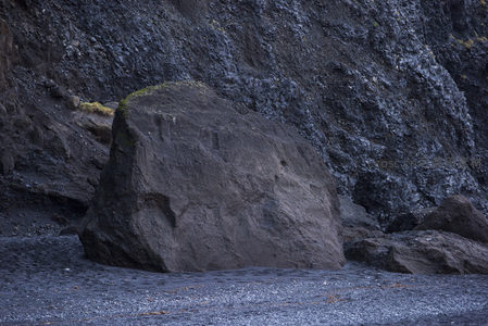 黑沙滩上孤石静卧岩壁前