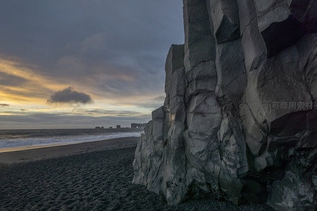 夕阳染金海岸，巨岩矗立黑沙滩前