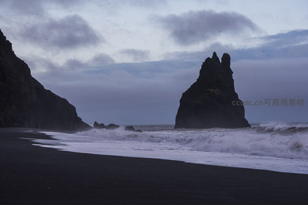 黑沙滩巨岩矗立，海浪拍岸云层低垂