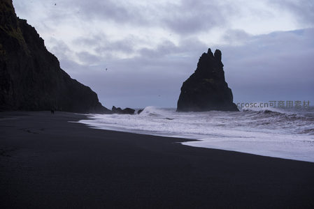 孤影黑岩立海边，浪涌沙岸鸟盘旋