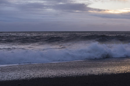 巨浪扑向黑沙岸，水花飞溅映霞光