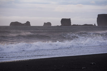 黑沙滩前浪花翻滚，远处礁石如沉默巨人