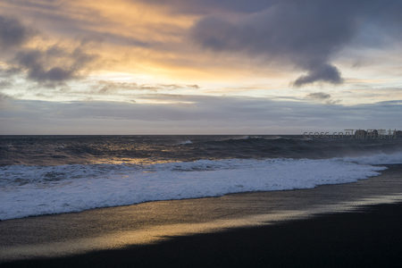 落日余晖下的黑沙海岸与浪涌
