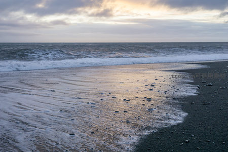 金色余晖下的黑沙滩潮汐痕迹
