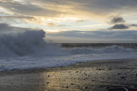 夕阳下的巨浪拍打黑色沙滩