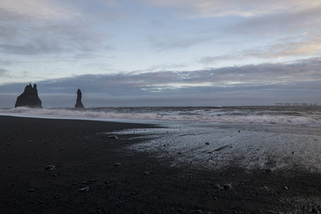 黑沙滩上的海浪与孤岩剪影