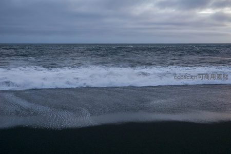 黑沙滩上浪花翻涌，阴云密布的海景