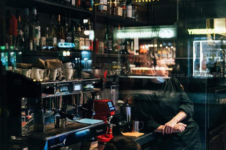 咖啡馆内咖啡师凝望窗外，夜色霓虹映窗