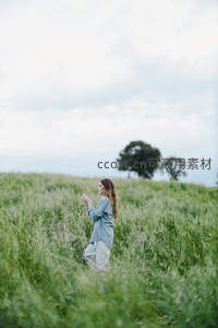 女子伫立麦田，手捧小花凝望远方