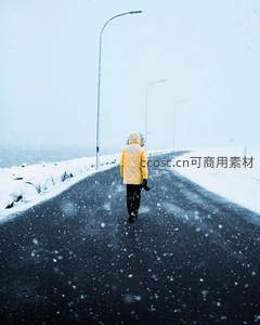 身穿黄色外套的人独行于飘雪公路