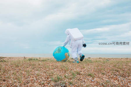 宇航员在海边拖动地球仪走向远方