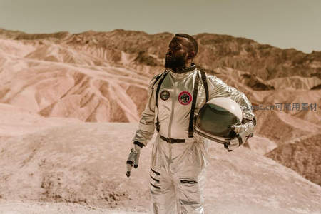 宇航员手持头盔站在荒漠星球表面
