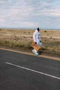 宇航员手持‘火星’标语行走在荒芜公路边