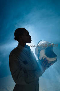 蓝光中托举头盔的宇航员剪影