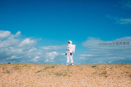 宇航员独自伫立海岸鹅卵石滩上