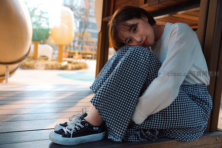 格纹裤少女蜷坐木台，阳光洒落