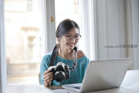 戴眼镜的女子手持相机在笔记本前微笑
