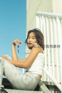 阳光下的时尚少女，手握墨镜倚栏而坐