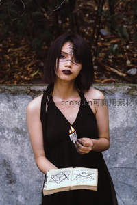 神秘黑衣女子手持咒术书与蜡烛