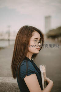 戴眼镜女孩手捧书本侧立