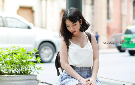 街头少女低头静坐城市一隅