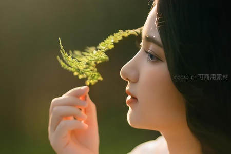 侧颜女子轻嗅绿叶，沐浴晨光温柔恬静