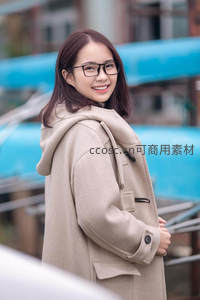 戴眼镜的女子微笑回眸，米色大衣显温柔气质