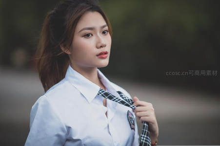 校服少女轻拉领带，眼神专注显青春活力