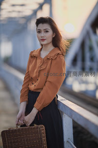 桥上女子提藤箱回眸，夕阳余晖映衬优雅身影
