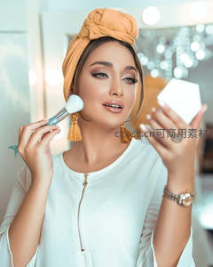 橙色头巾女子对镜轻扫腮红美妆