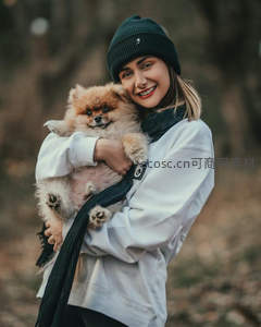 森林中怀抱博美犬的微笑女孩