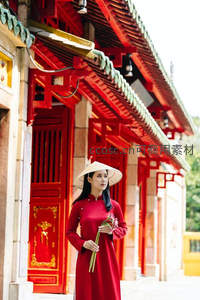 古寺红墙前，持花女子头戴斗笠若有所思