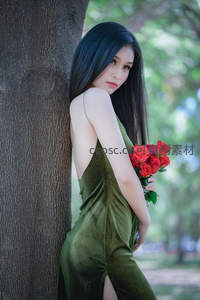 绿裙女子怀抱红玫瑰依偎大树